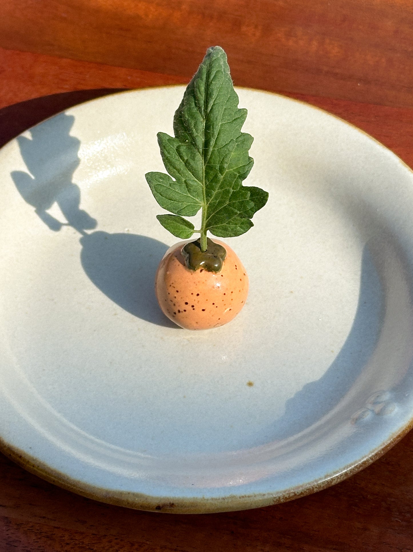 A mini speckled orange ceramic tomato vase with a tomato leaf