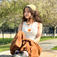 Chinese Vietnamese girl wearing a tank top, brown pants, and yellow bandana sits in a table looking to the side