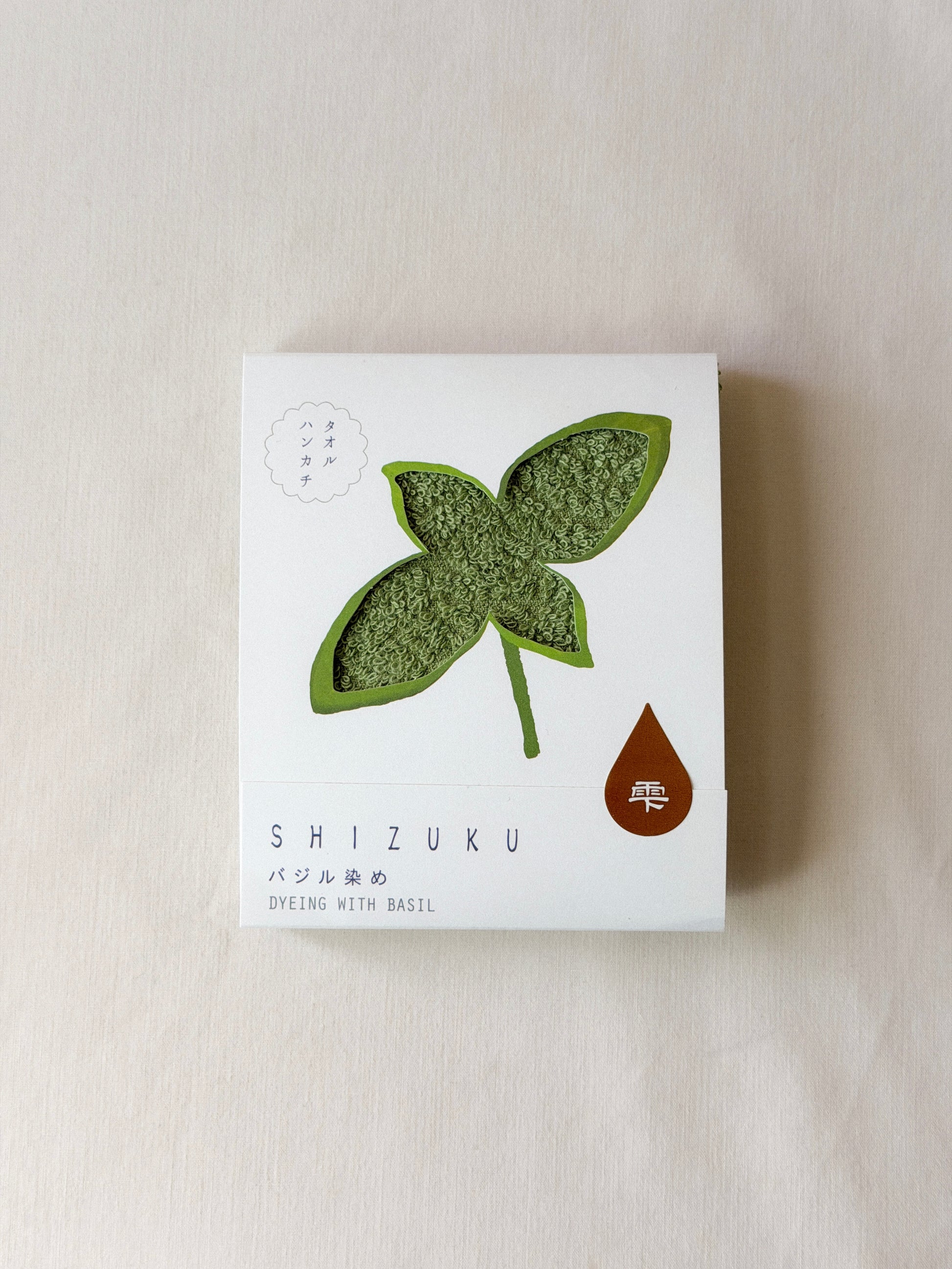 Packaged dark green towel with a cut-out of a basil