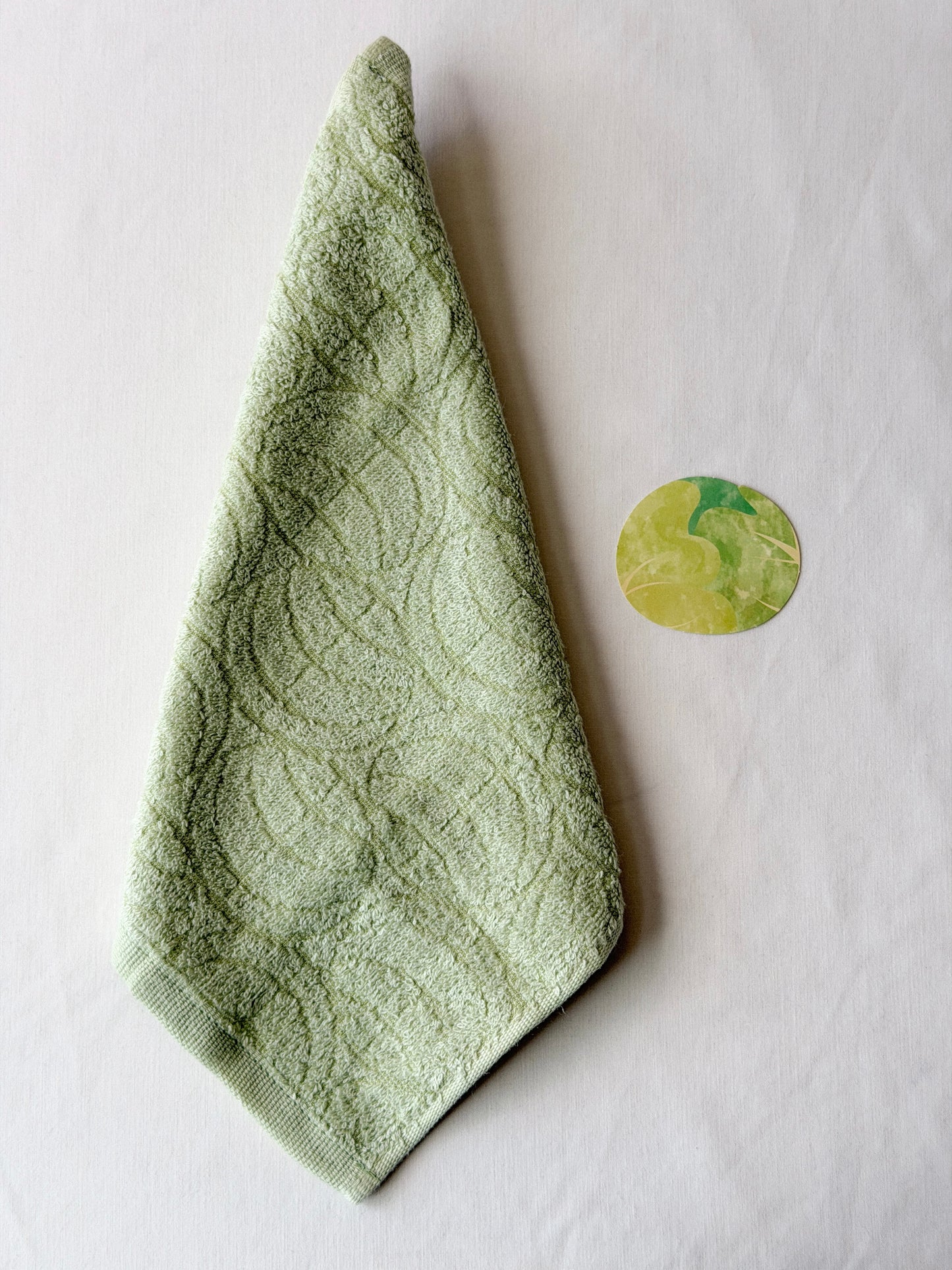 Light green towel with a cabbage illustration next to it on a white background