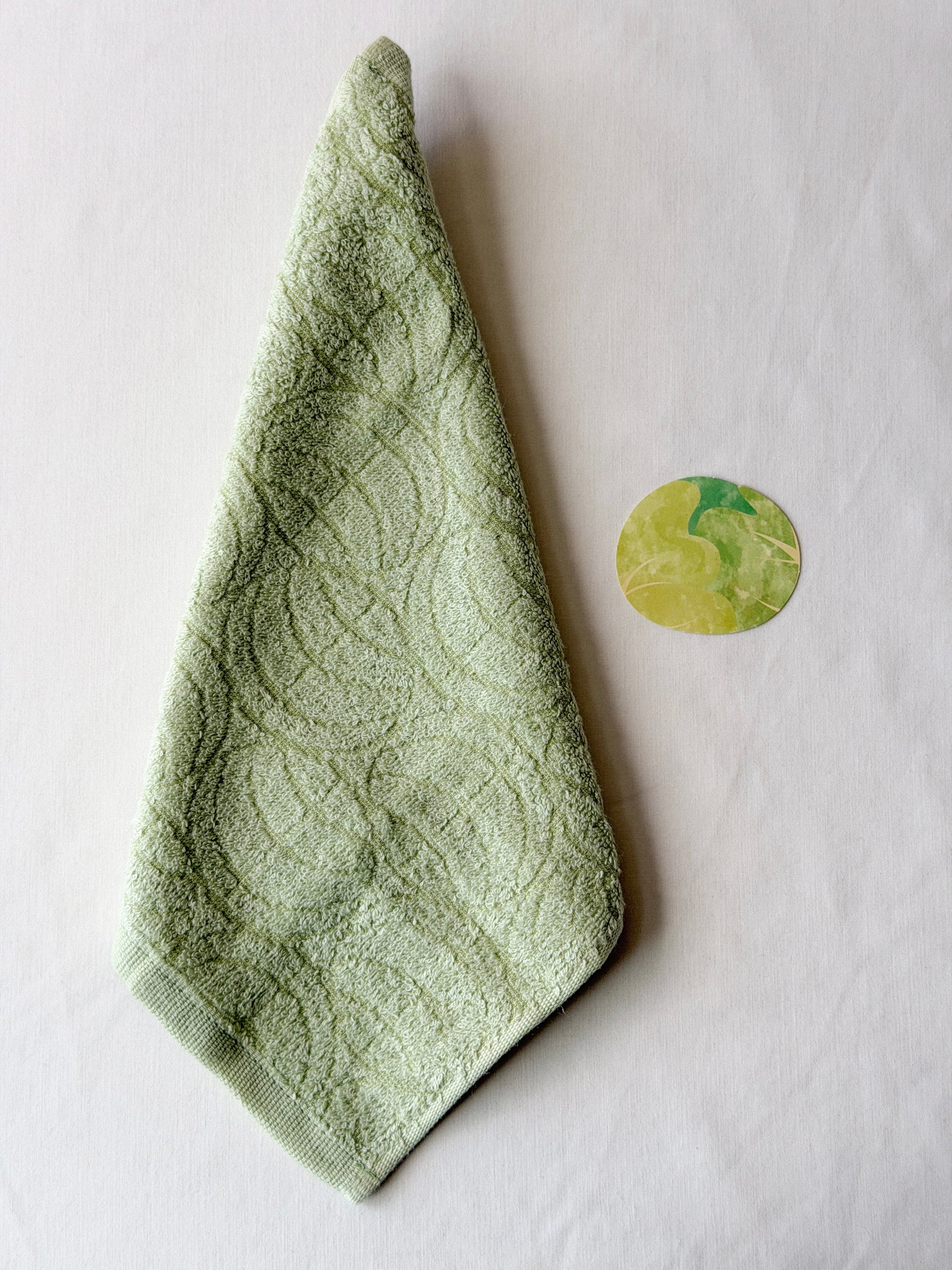 Light green towel with a cabbage illustration next to it on a white background