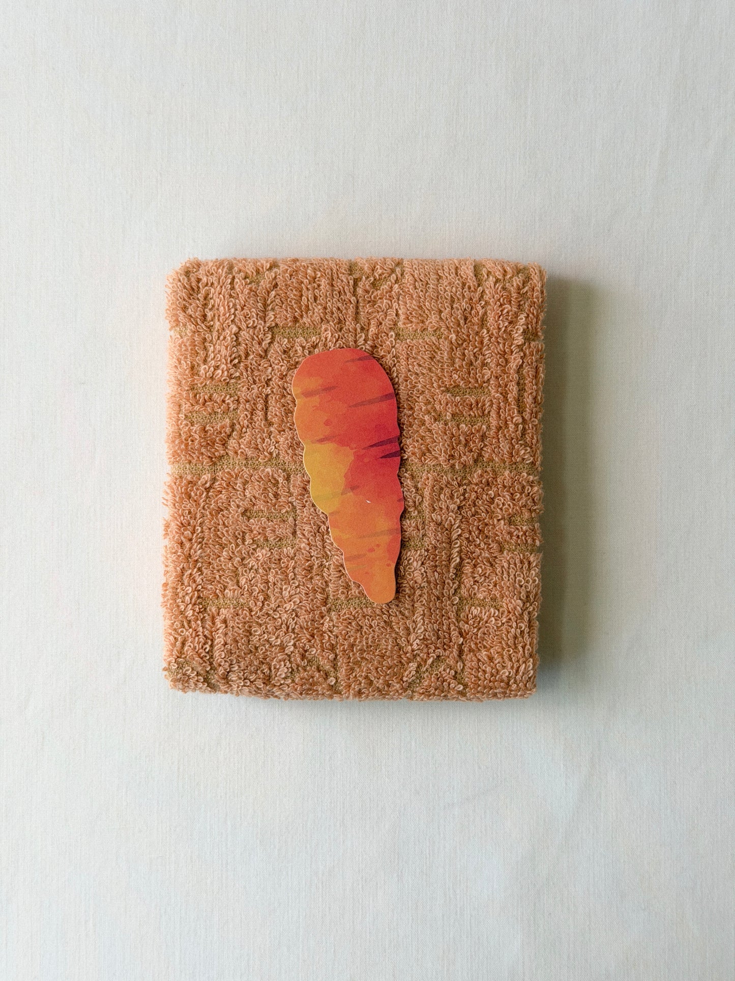Folded orange towel with a carrot illustration in the center on a white background