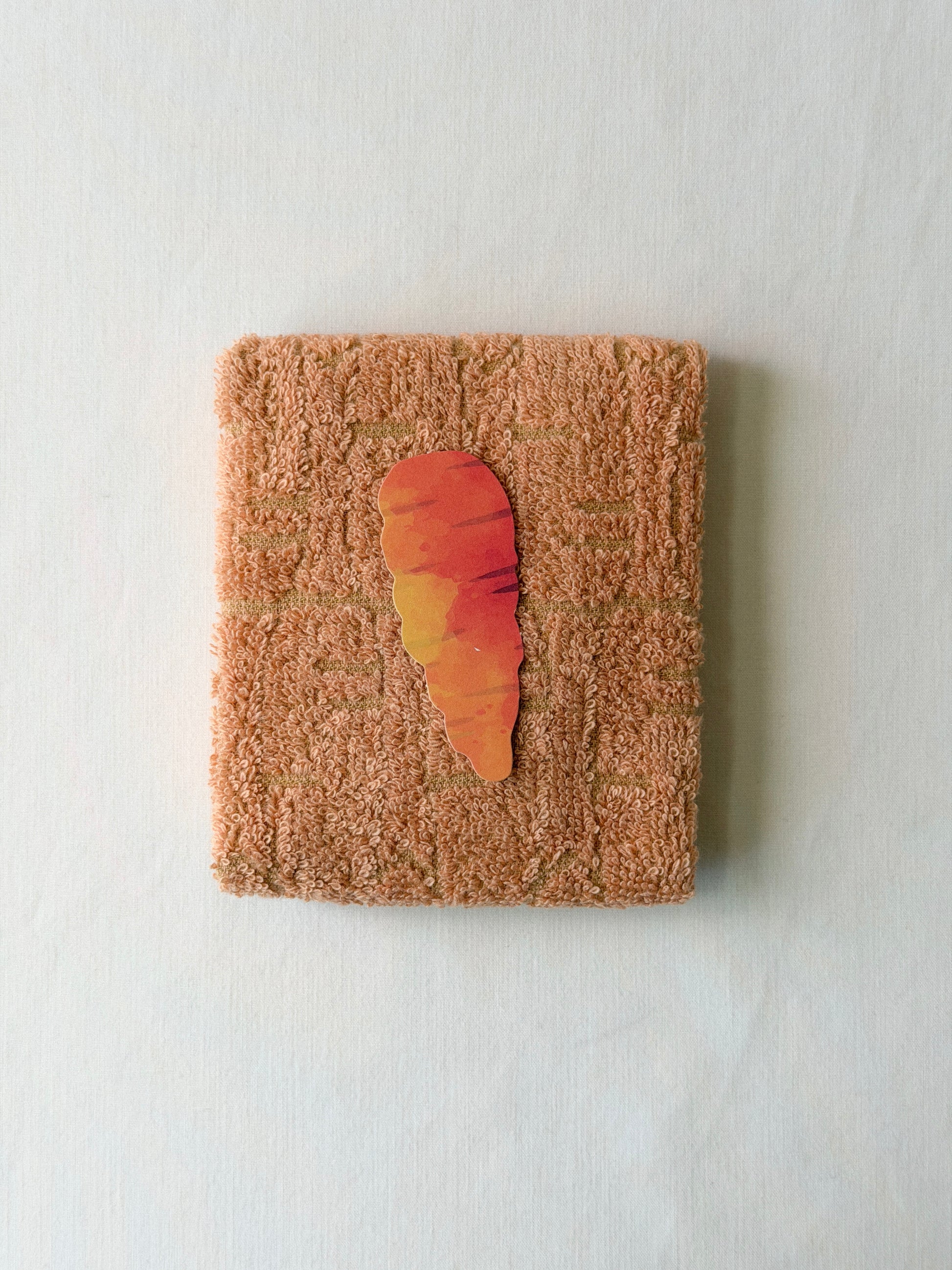 Folded orange towel with a carrot illustration in the center on a white background
