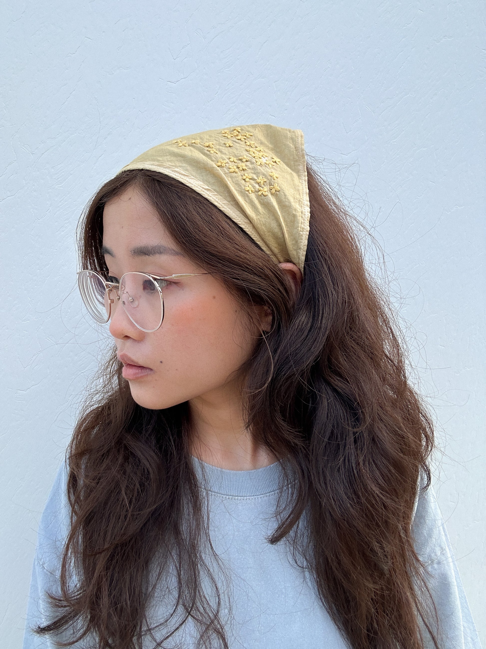 Person with long brown hair is wearing a yellow bandana tied around the top of their head and looking to the side