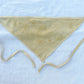 A muted yellow triangle-shaped bandana with two long straps and habe embroidered flowers lay on a white piece of cloth