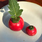Two small sizes of red ceramic tomato vases, the larger one with a tomato leaf stuck inside it