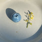 Mini ceramic blueberry vase next to a small branch of yellow flowers