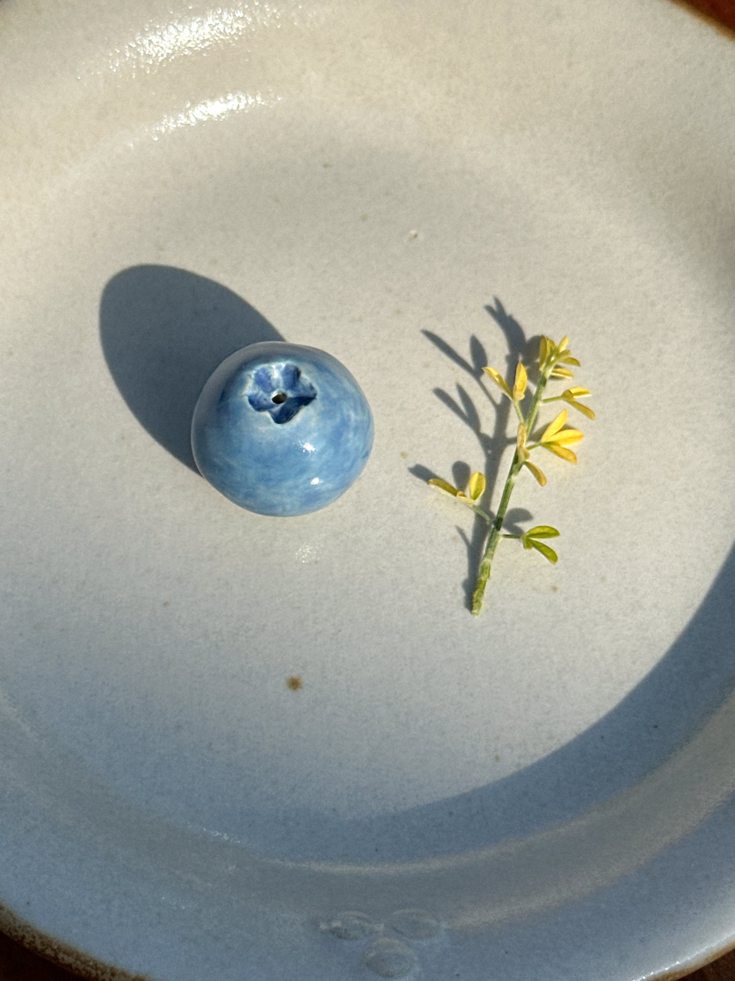Mini ceramic blueberry vase next to a small branch of yellow flowers