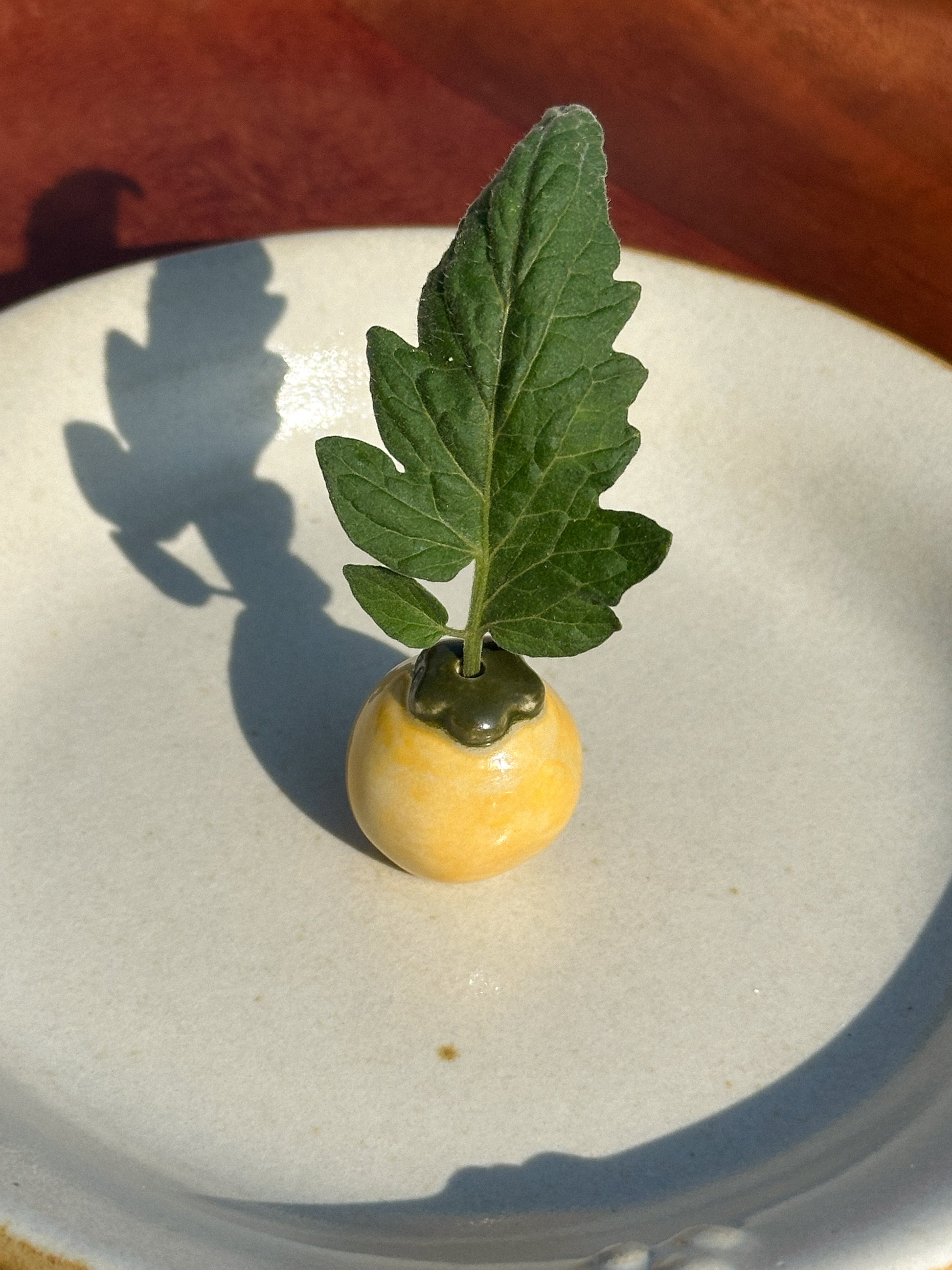 A mini yellow ceramic tomato vase with a tomato leaf 