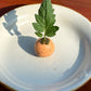 A mini speckled orange ceramic tomato vase with a tomato leaf 