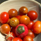 A bowl of red cherry tomatoes and one mini ceramic tomato vase