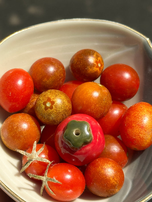 A bowl of red cherry tomatoes and one mini ceramic tomato vase