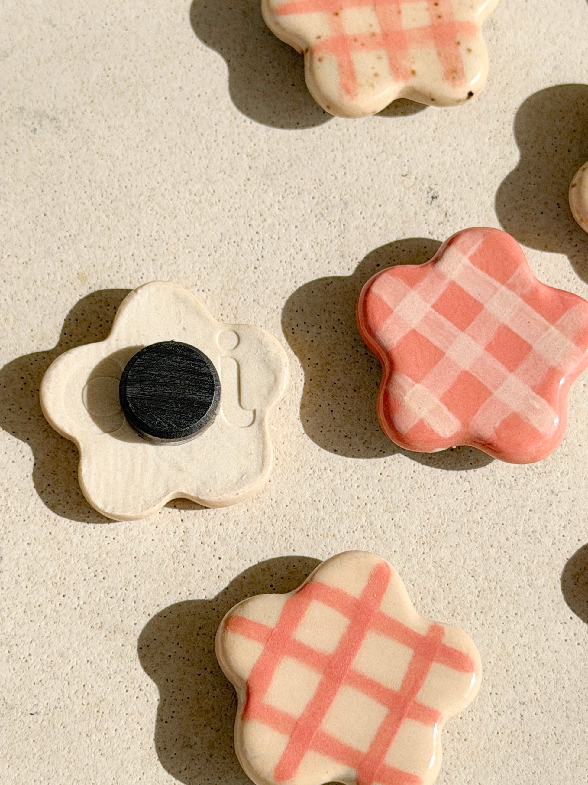 Flower-shaped ceramic magnets with four different checkered design in ivory and pink, some show the back with the magnet