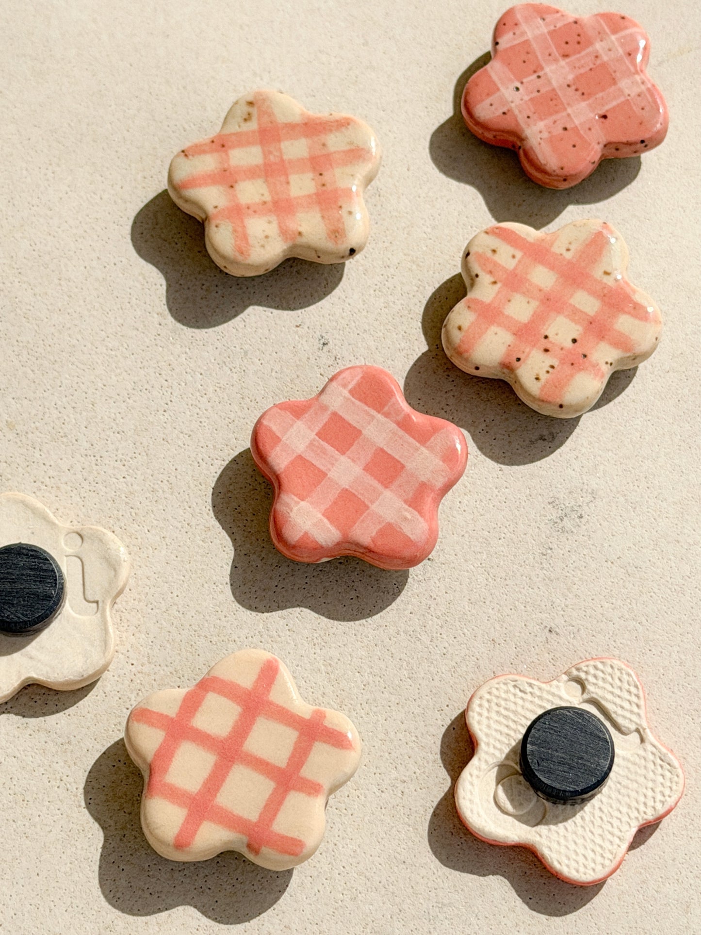 Flower-shaped ceramic magnets with four different checkered design in ivory and pink, some show the back with the magnet