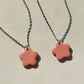 Partial view of two stainless steel necklaces with a glossy floral shaped pink ceramic pendant