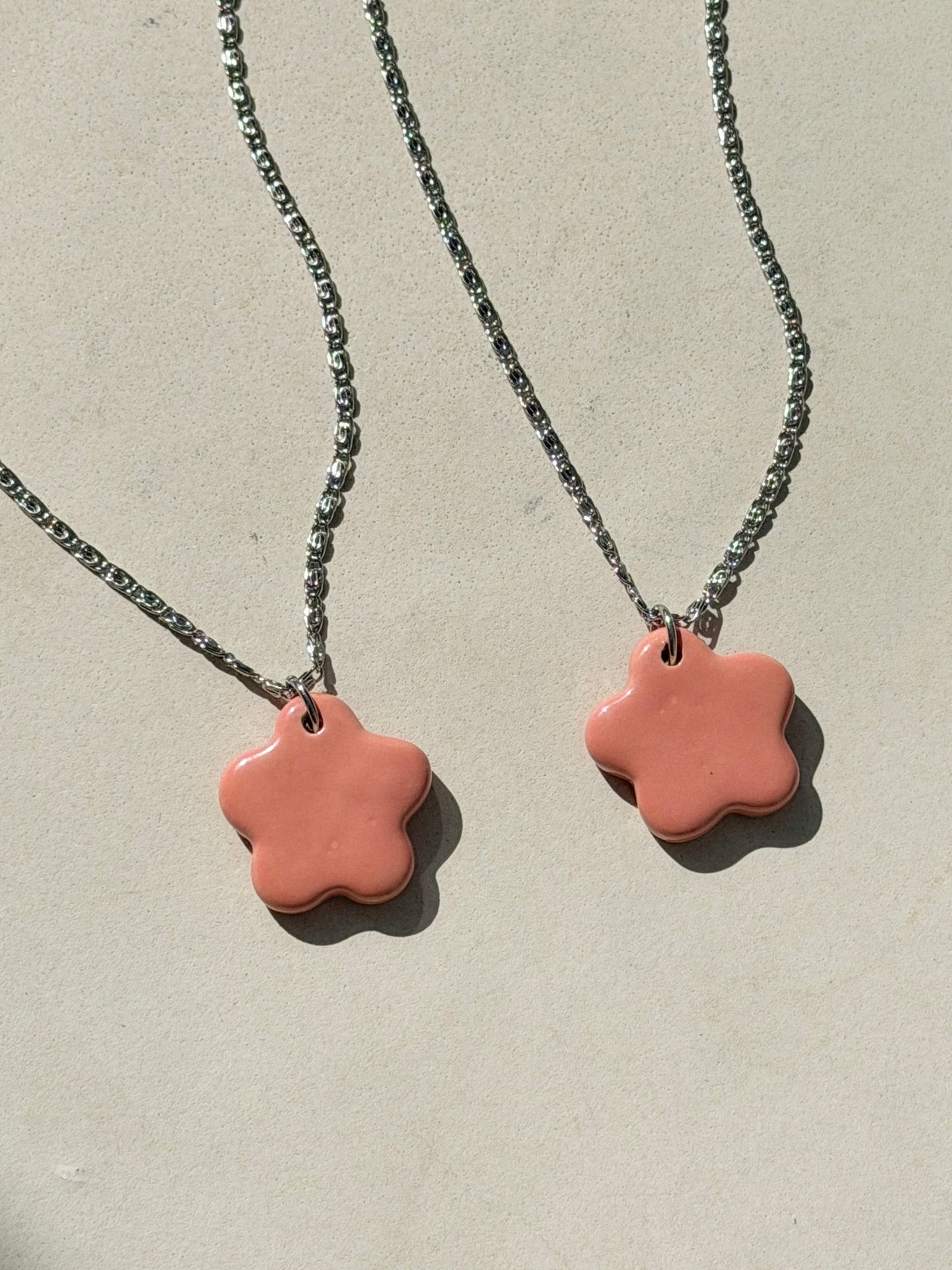 Partial view of two stainless steel necklaces with a glossy floral shaped pink ceramic pendant