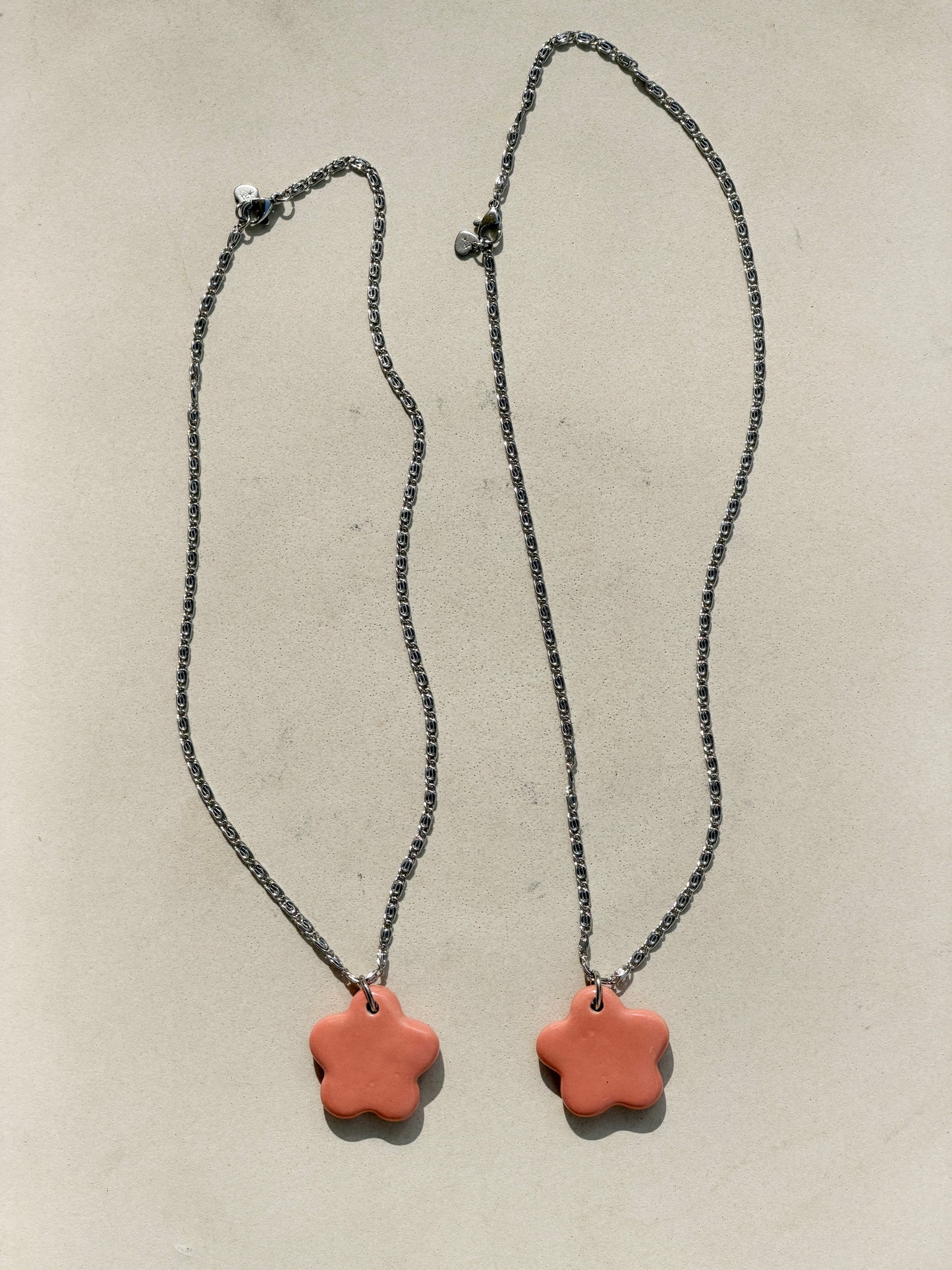 Full view of two stainless steel necklaces with a glossy floral shaped pink ceramic pendant