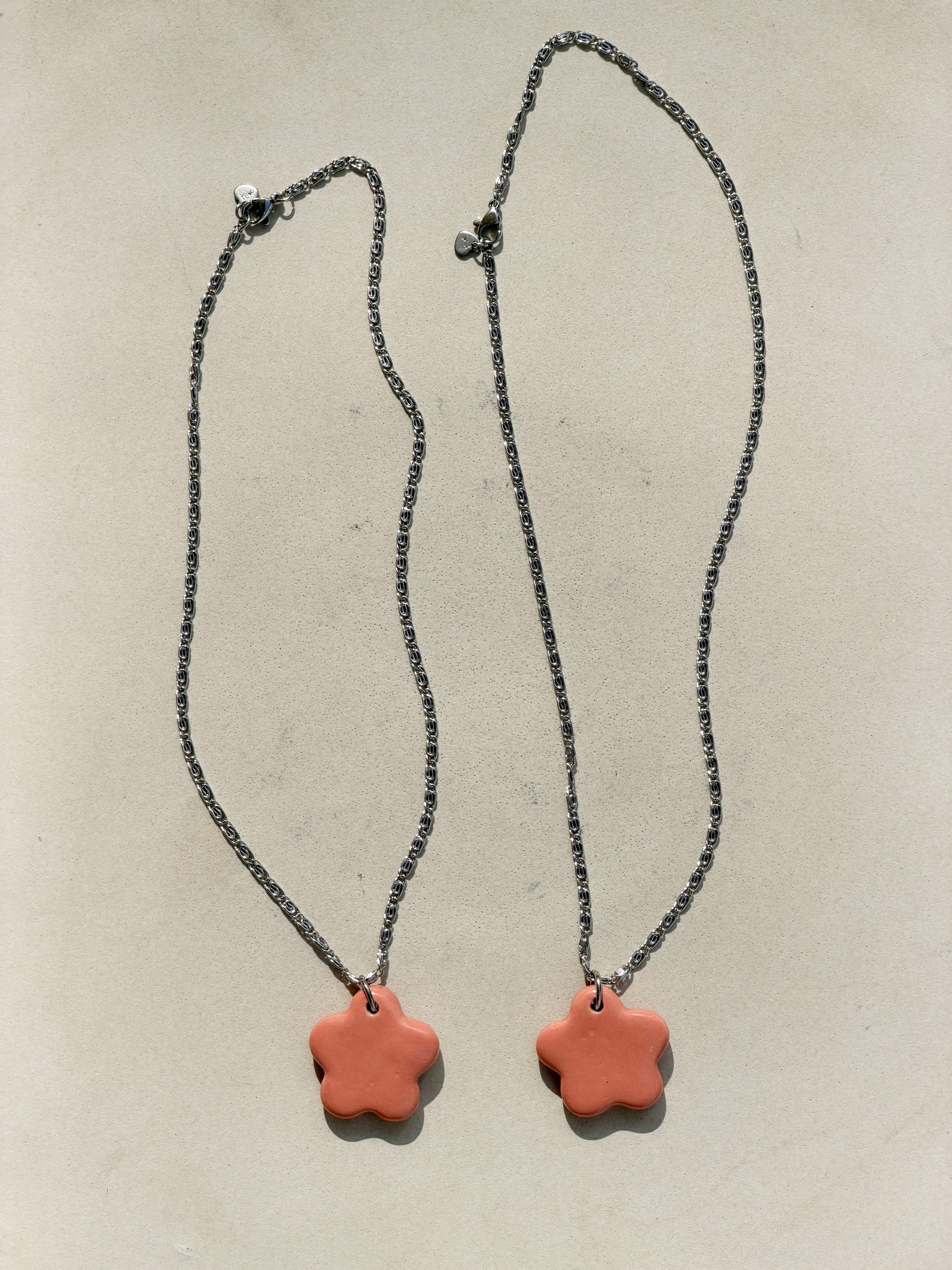 Full view of two stainless steel necklaces with a glossy floral shaped pink ceramic pendant