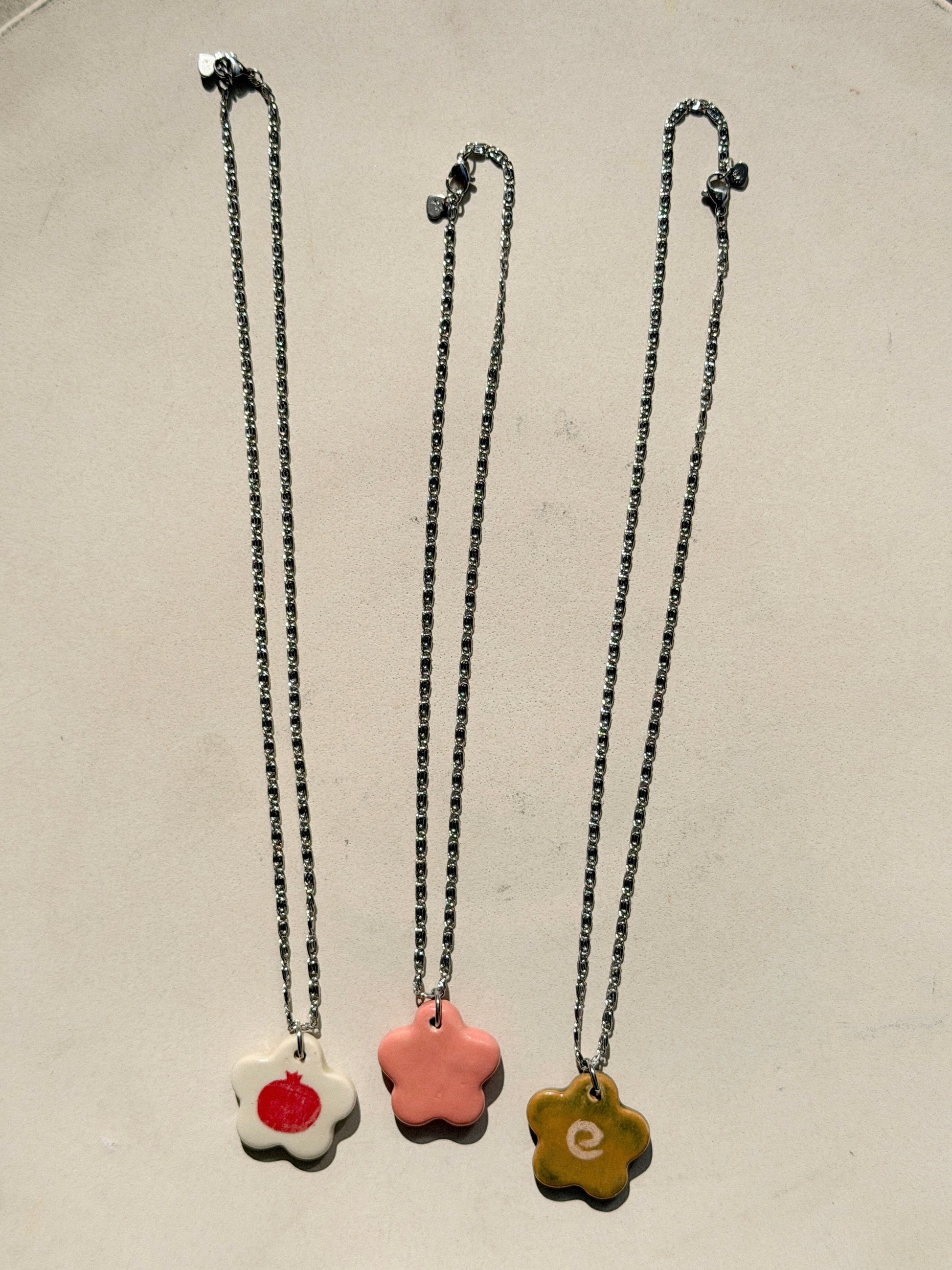 Full image of three necklaces, each one featuring a stainless steel chain made of tiny swirls and a glossy floral-shaped ceramic charm with different designs