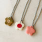 Partial view of three necklaces, each one featuring a stainless steel chain made of tiny swirls and a glossy floral-shaped ceramic charm with different designs
