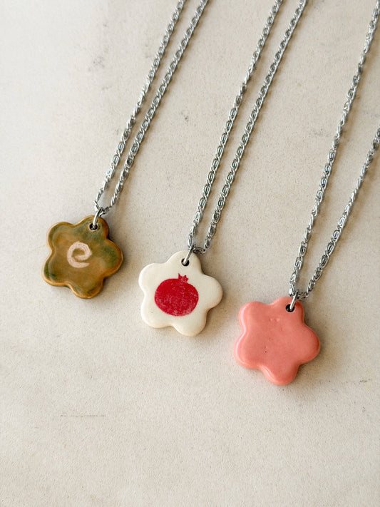 Partial view of three necklaces, each one featuring a stainless steel chain made of tiny swirls and a glossy floral-shaped ceramic charm with different designs