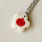 Stainless steel necklace with an off-white floral-shaped ceramic pendant featuring a distressed red pomegranate in the center