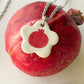 On top of a pomegranate lies a necklace with an off-white  floral-shaped ceramic pendant featuring a red pomegranate drawing