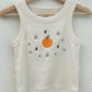 A beige sleeveless tank top with embroidered tangerine, flowers, and Chinese characters for luck hang on a wooden clothes hanger