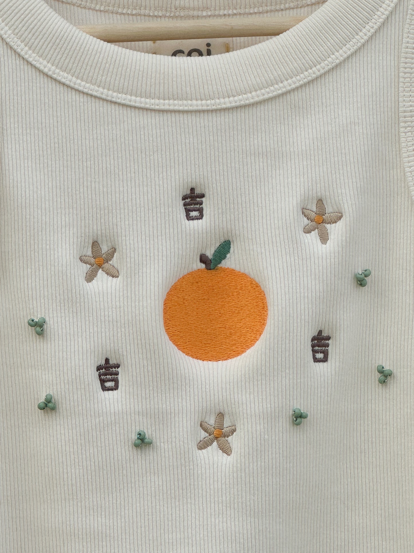 Up-close image of the design of the tank top, showing embroidered tangerine, flowers, and Chinese characters for luck and hand-sewn clusters of beads