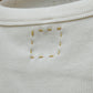 Up-close image of the hand-embroidered box on the top back of a beige tank top.