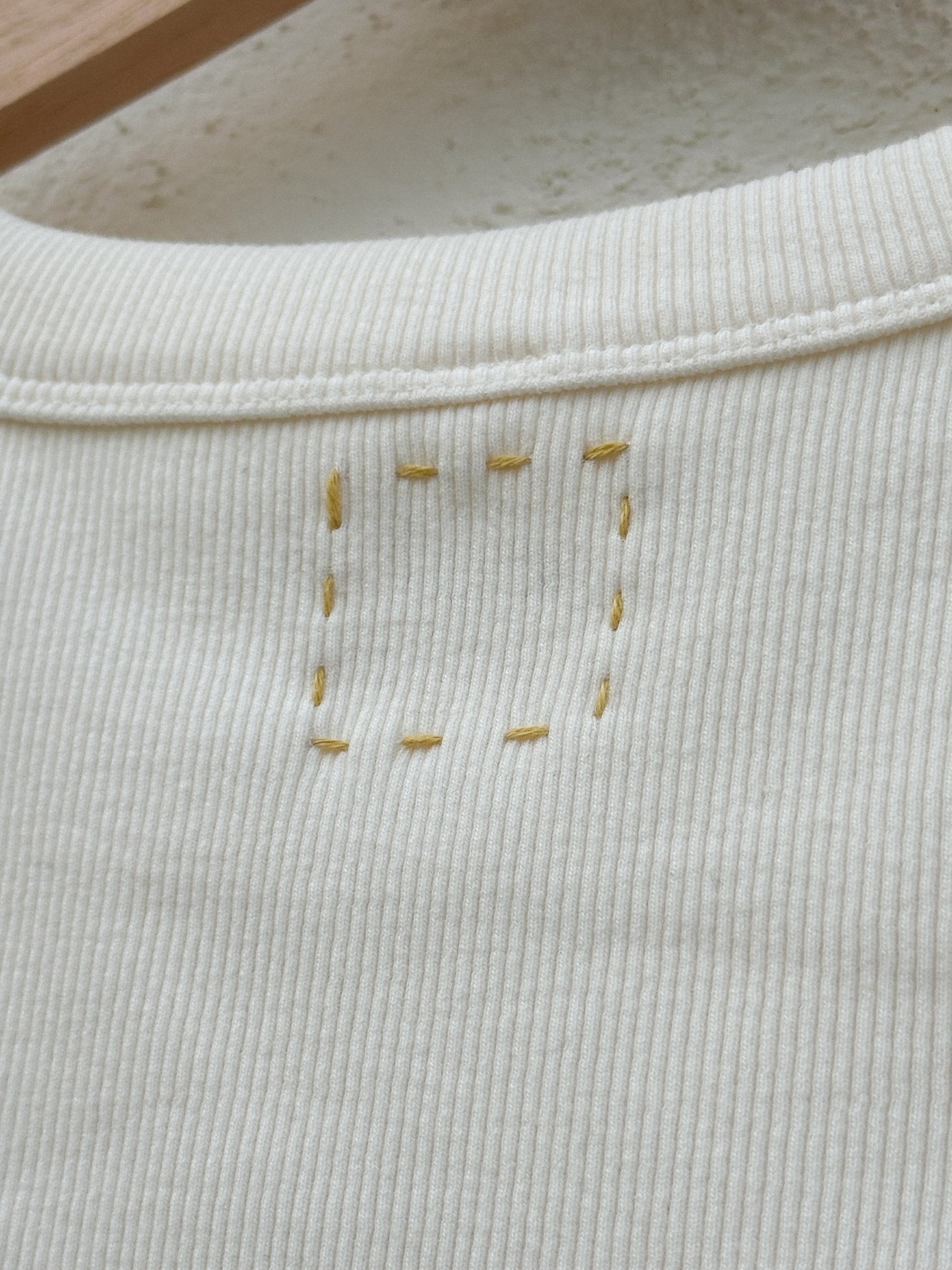 Up-close image of the hand-embroidered box on the top back of a beige tank top.