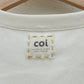 Up-close image of the inside of the beige tank top, showing a logo label for "coi" hand-embroidered on with yellow thread.