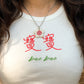 Close-up of person wearing a white baby tee with the Chinese words 寶寶 and "bao bao" on it and a necklace with a flower-shaped ceramic pendant featuring a pomegranate