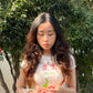 Woman with long hair wearing a white baby tee with the Chinese words 寶寶 and "bao bao" on it and holding pomegranate leaves in front of a pomegranate tree