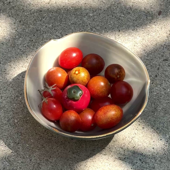 A bowl of red cherry tomatoes and one mini ceramic tomato vase