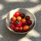 A bowl of red cherry tomatoes and one mini ceramic tomato vase