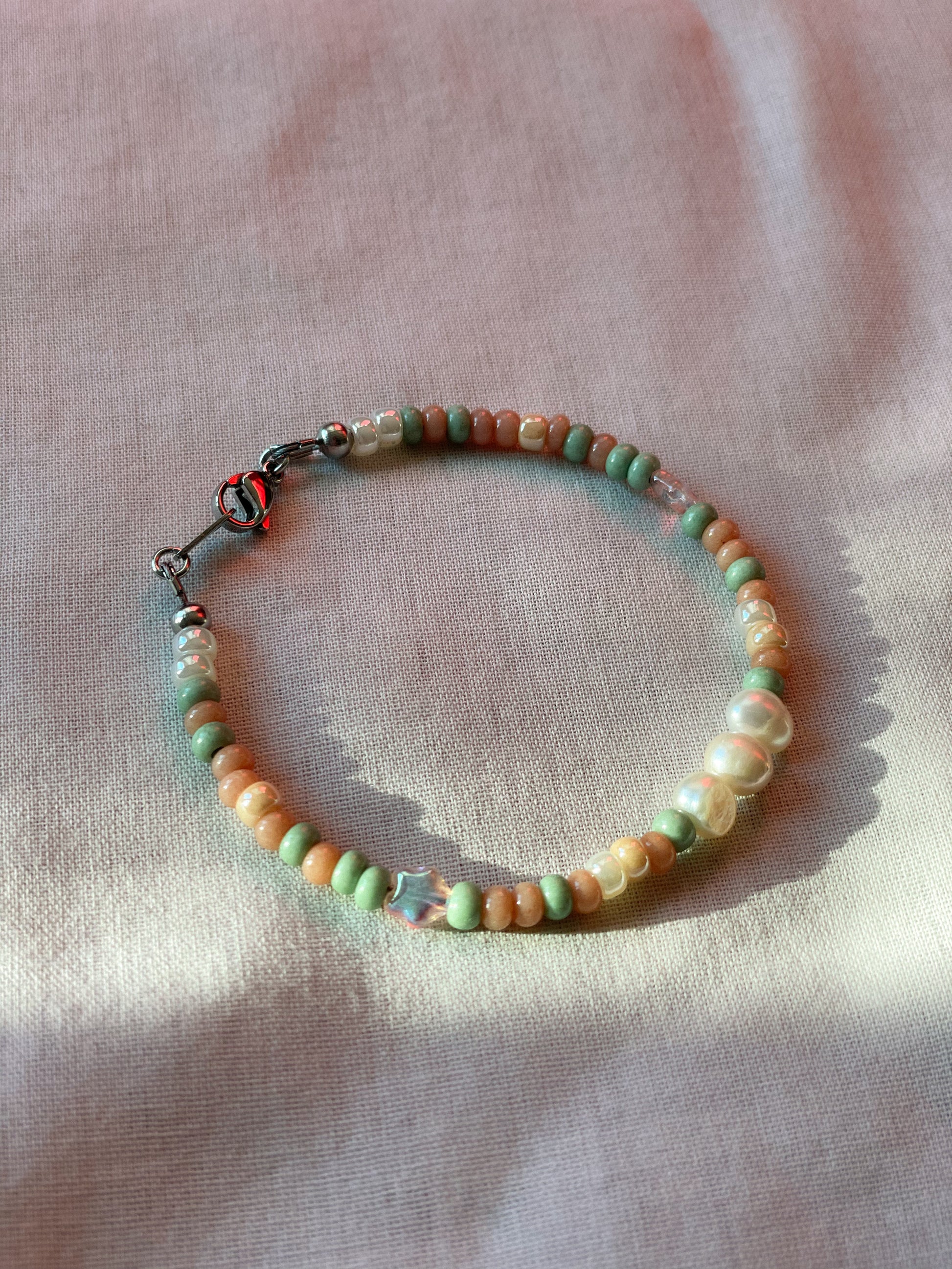 A bracelet made of Czech glass beads, white freshwater pearls, and stainless steel lay flat on a white piece of cloth.