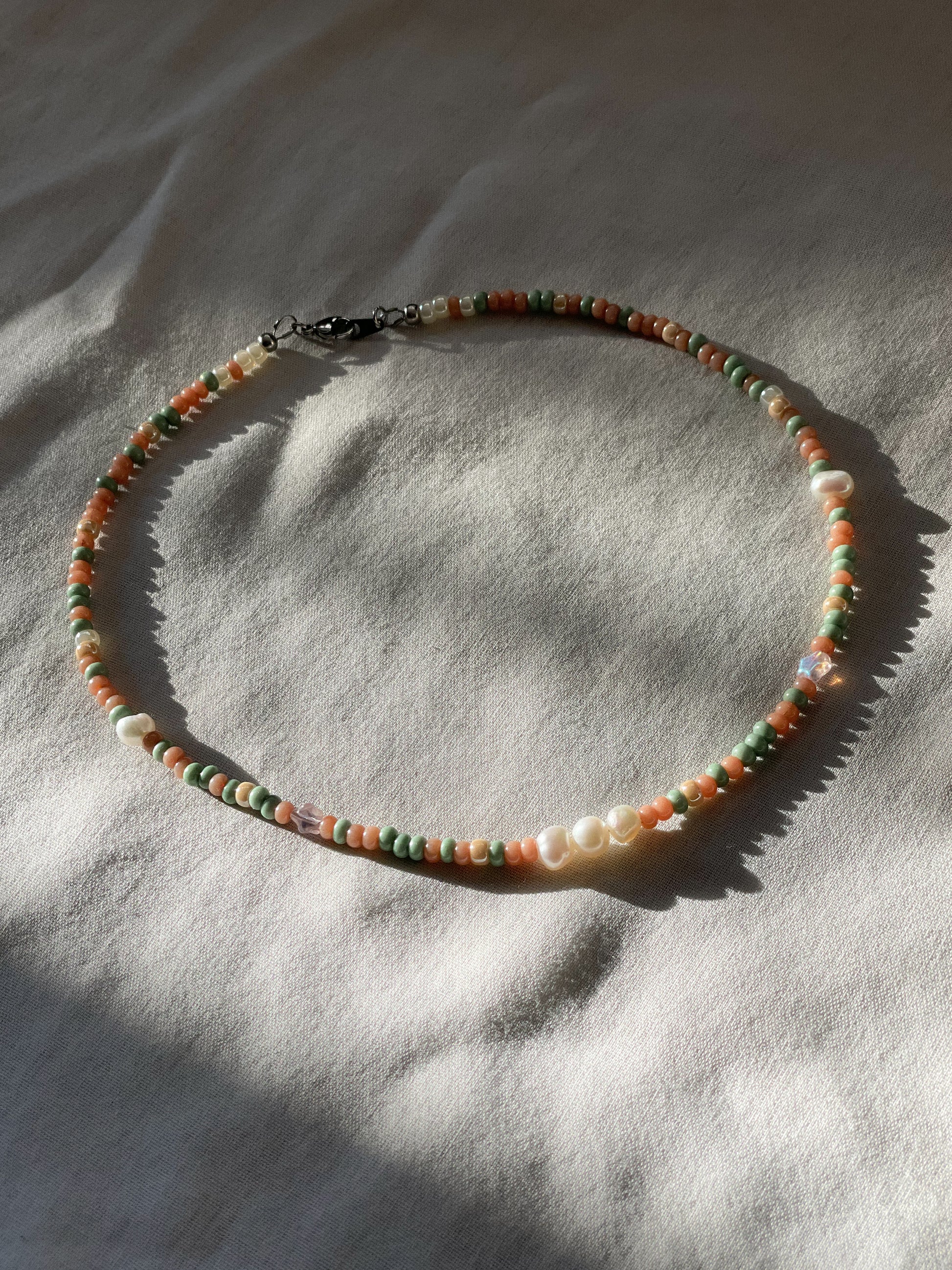 A necklace made of Czech glass beads, white freshwater pearls, and stainless steel lay flat on a white piece of cloth.