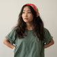 A Chinese Vietnamese woman with long hair wearing a green t-shirt and blue jeans with her face turned slightly to the side and looking into the distance. Her hands are on her waist.