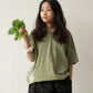 A Chinese Vietnamese woman wearing a yellow green t-shirt and black shorts stands with her back to the camera. She’s holding a bunch of tong ho in one hand.