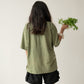 A Chinese Vietnamese woman wearing a yellow green t-shirt and black shorts stands with her back to the camera. She’s holding a bunch of tong ho in one hand.