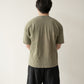 A Chinese man wearing a yellow brownish green t-shirt and black shorts stands with his back to the camera.