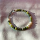 A bracelet made of jade, Japanese glass beads, white freshwater pearls, and stainless steel lay flat on a white piece of cloth.