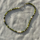 A necklace made of jade, Japanese glass beads, white freshwater pearls, and stainless steel lay flat on a white piece of cloth in the sunlight.
