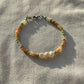 A bracelet made of Czech glass beads, white freshwater pearls, and stainless steel lay flat on a white piece of cloth in the sunlight.