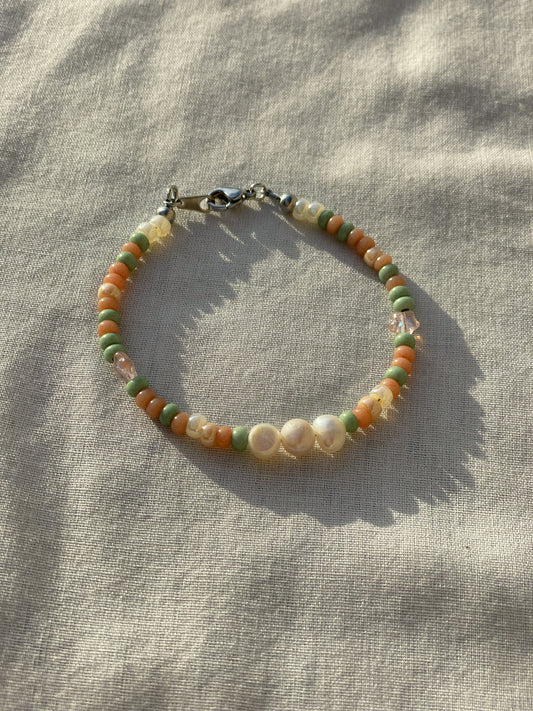 A bracelet made of Czech glass beads, white freshwater pearls, and stainless steel lay flat on a white piece of cloth in the sunlight.