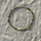 A necklace made of jade, Japanese glass beads, white freshwater pearls, and stainless steel lay flat on a white piece of cloth in the sunlight.