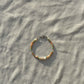 A bracelet made of Czech glass beads, white freshwater pearls, and stainless steel lay flat on a white piece of cloth in the sunlight.