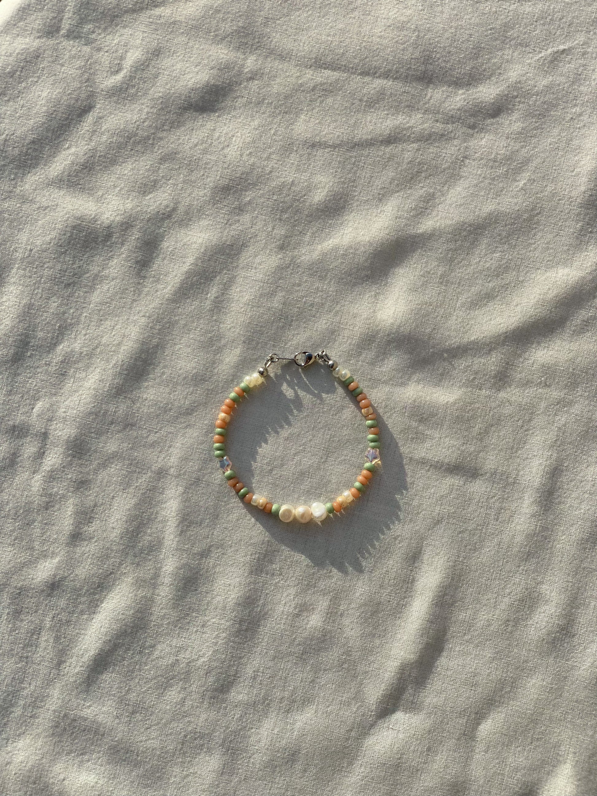 A bracelet made of Czech glass beads, white freshwater pearls, and stainless steel lay flat on a white piece of cloth in the sunlight.